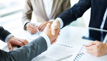 Image of business partners handshaking over business objects on workplace
